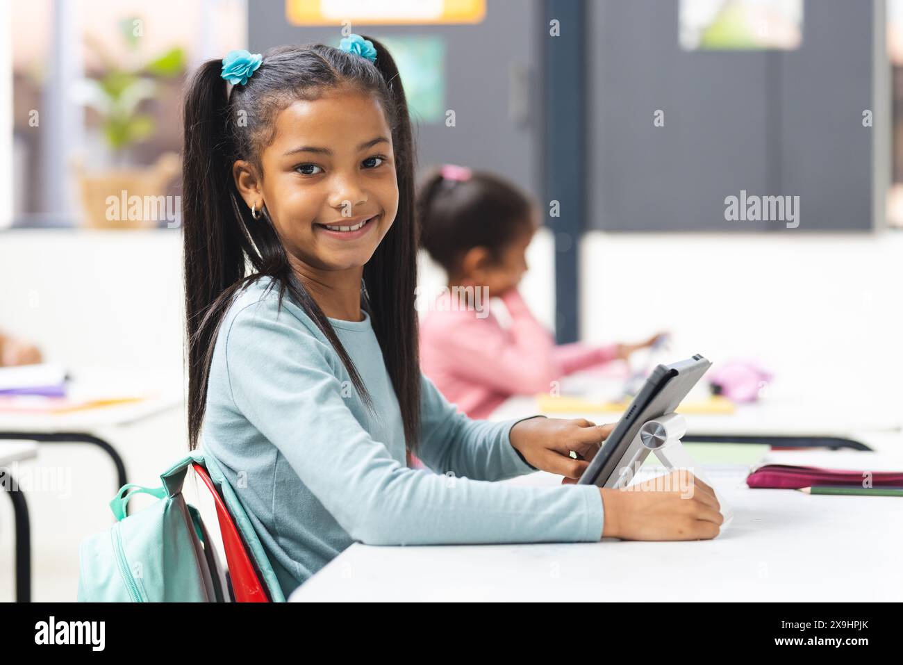 In school, young biracial girl holding tablet smiles at camera in ...