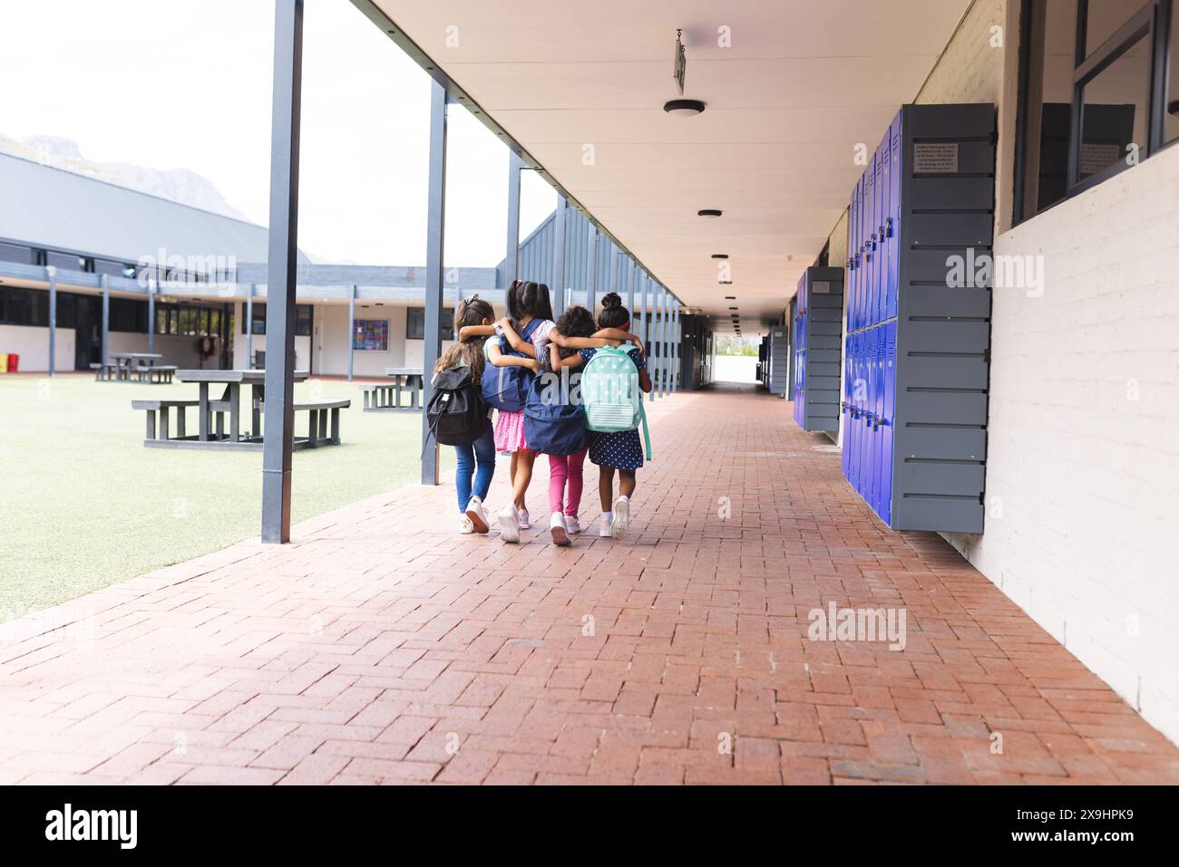 In school, four young biracial girls are walking together outdoors, copy space Stock Photo