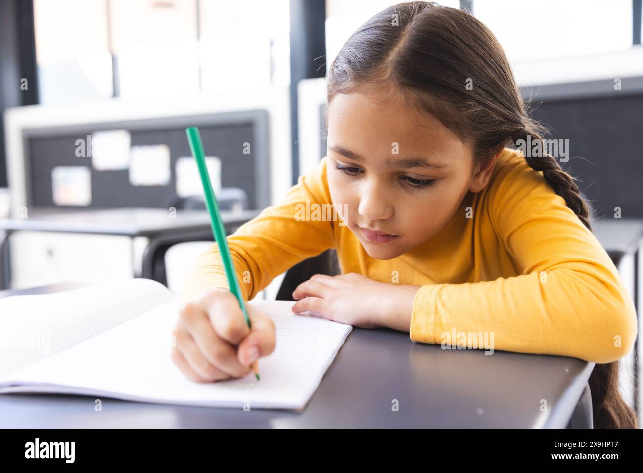 In school, young biracial girl with light brown skin focusing on writing in the classroom Stock Photo