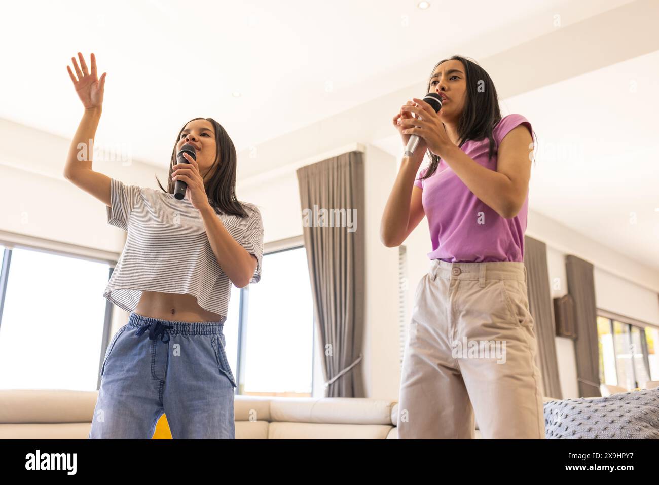Biracial young sisters, holding microphones, singing at home Stock Photo