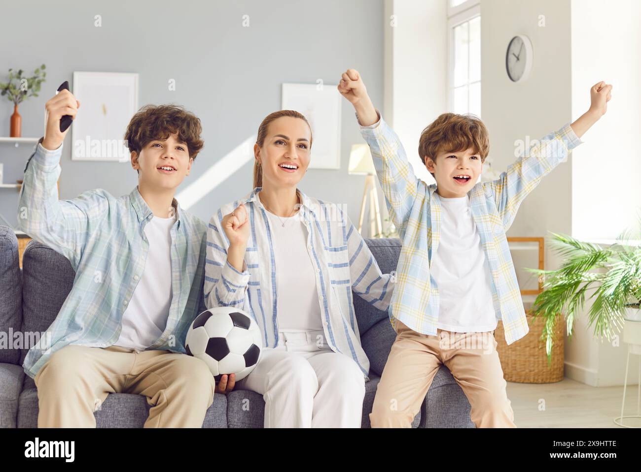 Mother sitting on sofa with her children and watching football match on tv in living room at home. Stock Photo