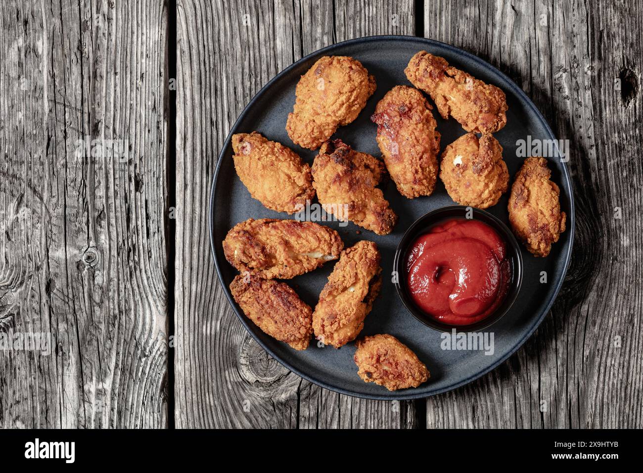 overhead view of american style crispy fried chicken wings on dark plate with ketchup on rustic wooden table, horizontal view from above, flat lay, fr Stock Photo