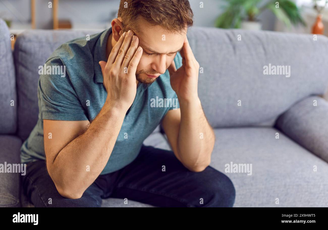 Man Suffering From Headache On Sofa At Home Stock Photo