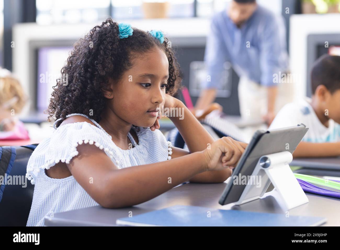 In school, in the classroom, a young biracial girl with curly hair is using a tablet Stock Photo