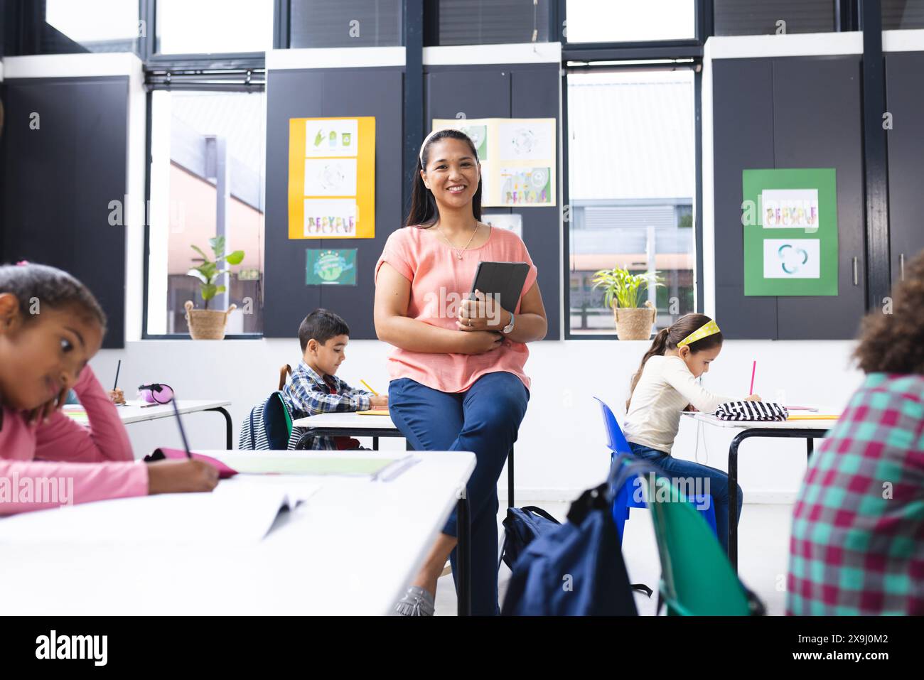 In school, young biracial female teacher smiles holding a tablet in the ...