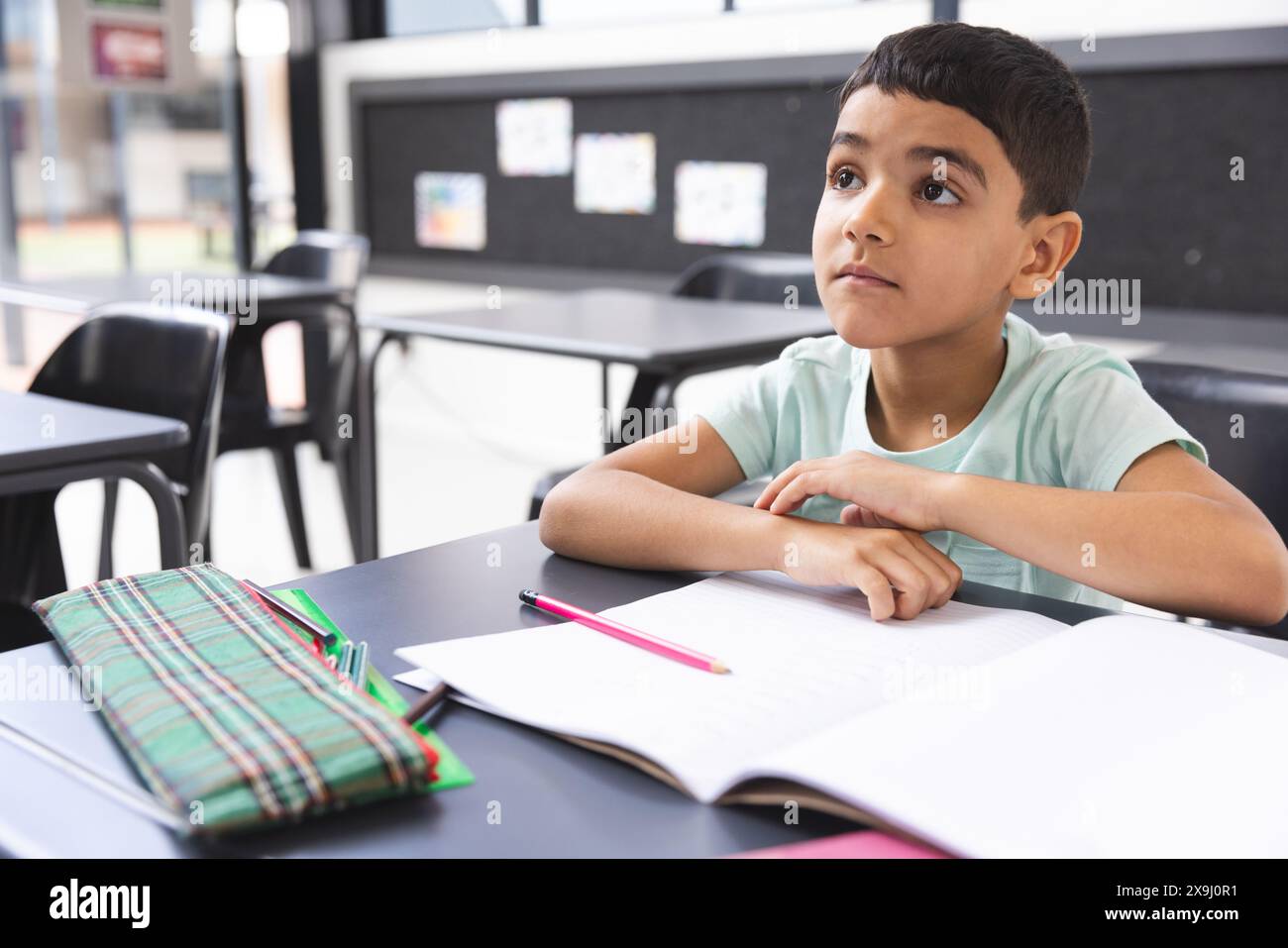 In school, young biracial boy sitting at a desk in a classroom, looking ...