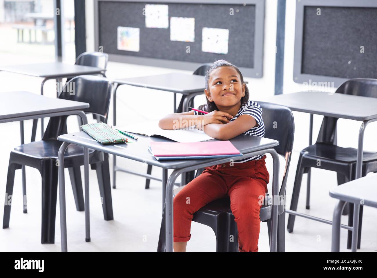 In school, young biracial girl with a thoughtful look sitting at a desk ...