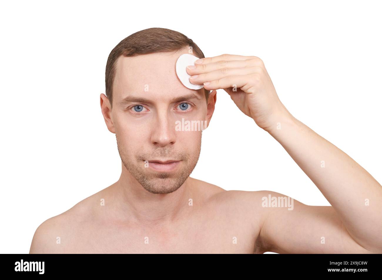 Man doing home skin care routine. Cotton pad near male forehead. Dermatology treatment. Cream facial apply. Cosmetology guy portrait. Cleaning lotion. Skincare hygiene. Copyspace. Isolated on white Stock Photo