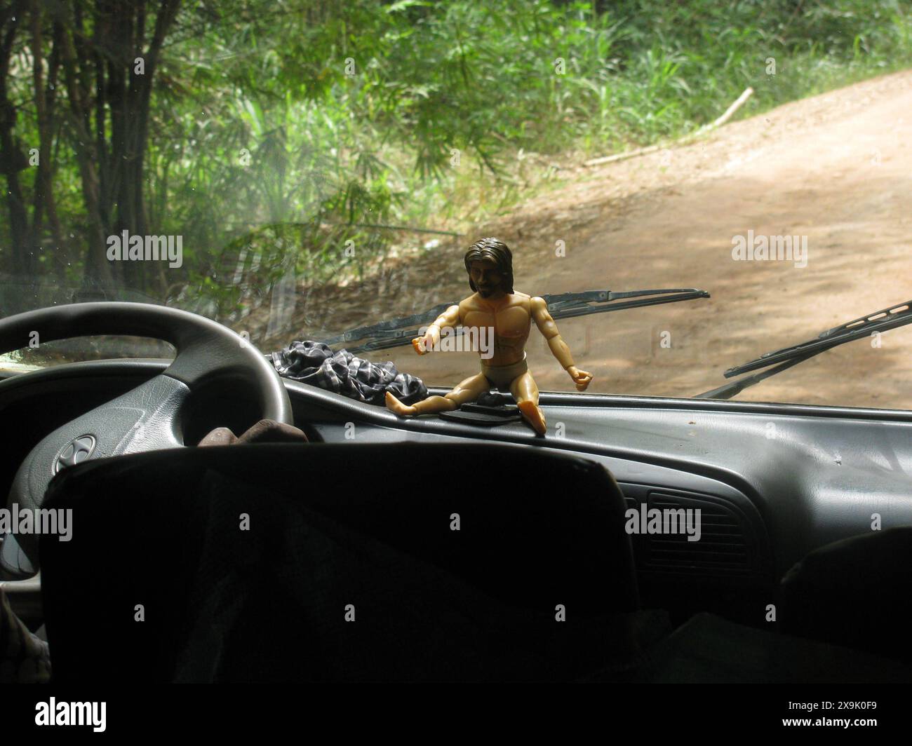 A whimsical shot of a Jesus action figure sitting on a car dashboard ...