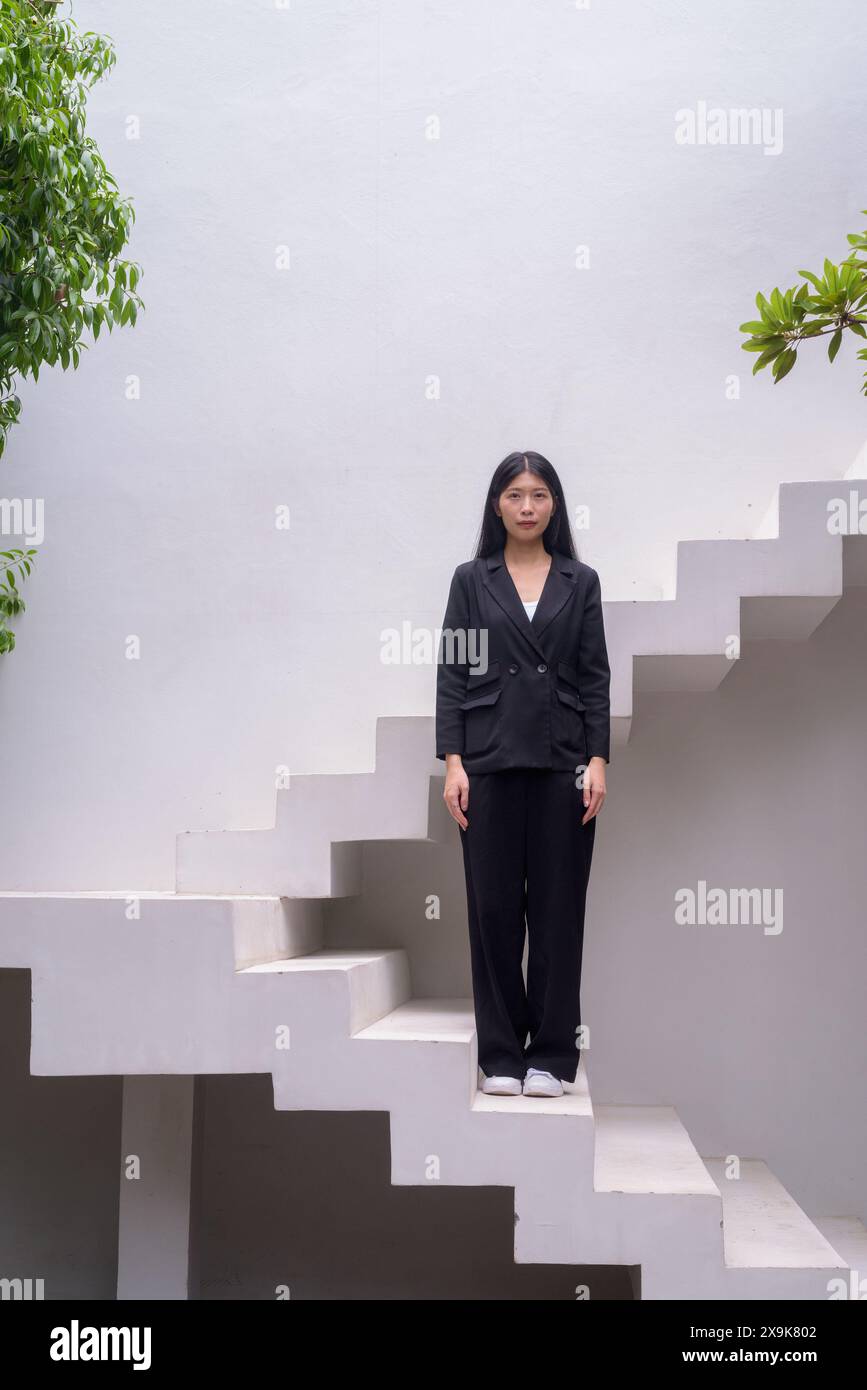 Full body portrait of a professional woman in business attire exuding confidence on modern architectural steps including greenery Stock Photo