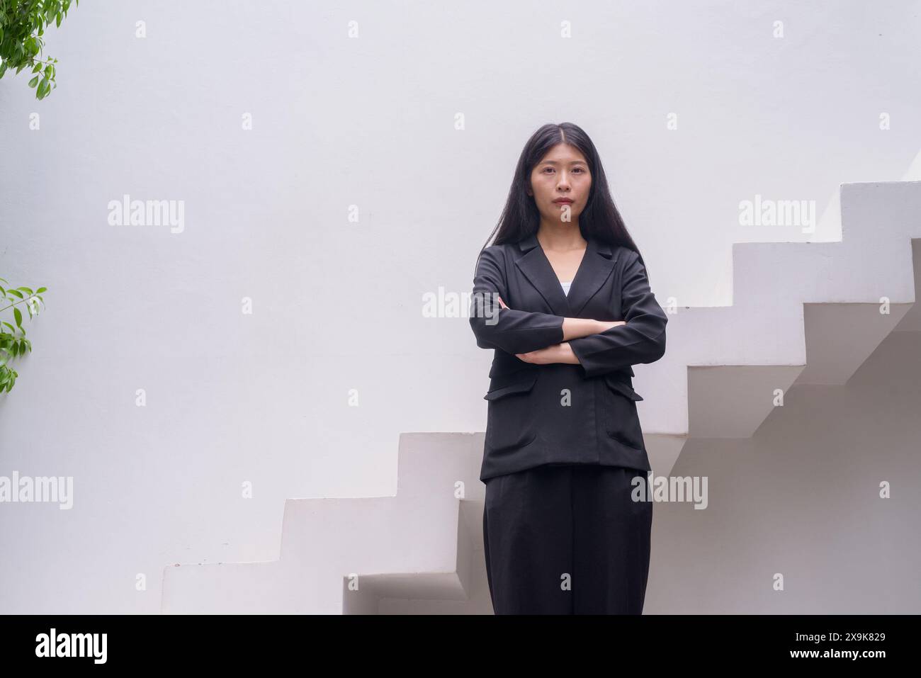 Portrait of a professional woman in business attire exuding confidence on modern architectural steps including greenery with arms crossed Stock Photo
