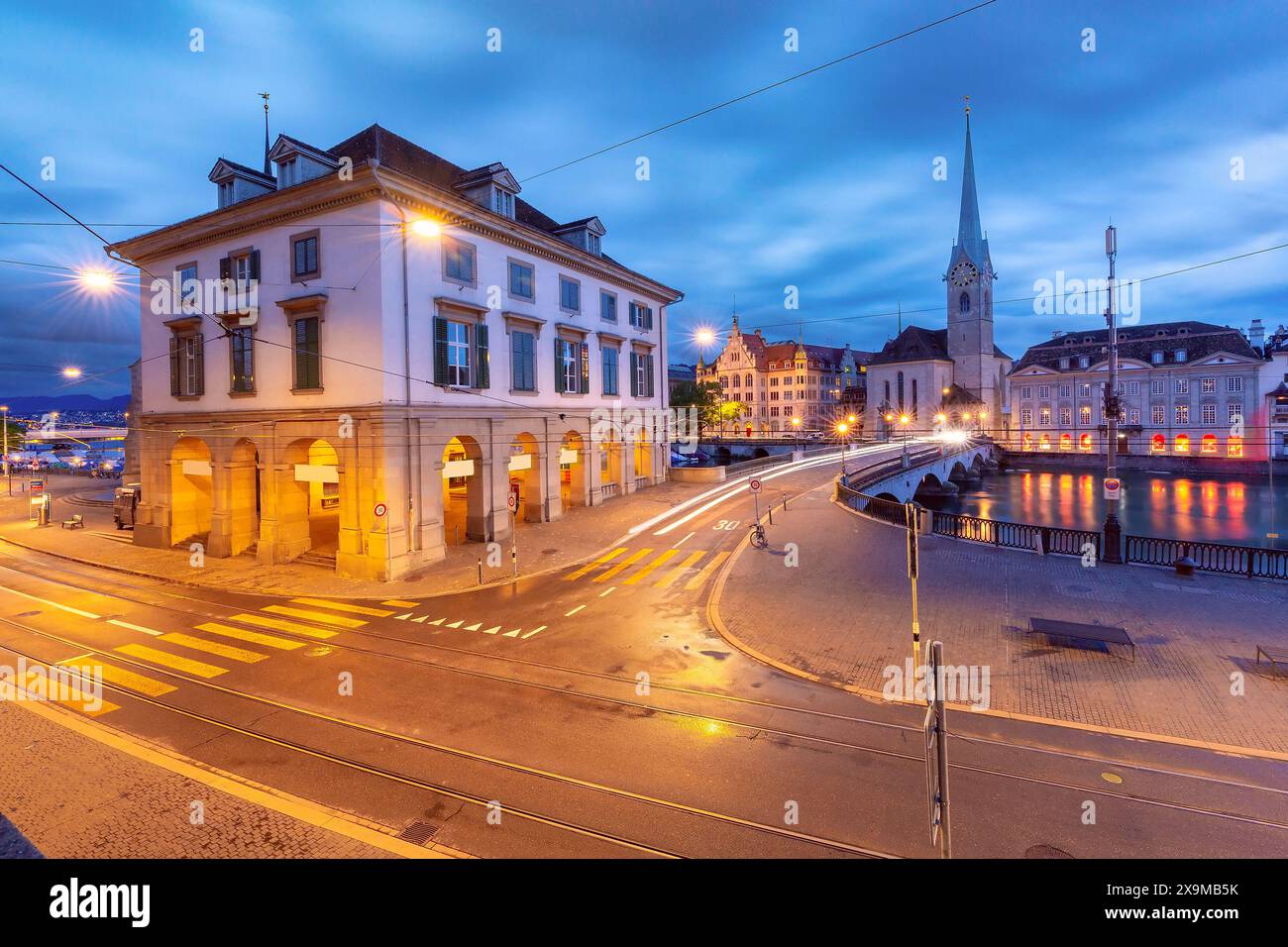 Panoramic evening view of Fraumunster and Munsterbrucke with illuminated streets in Zurich, Switzerland. Stock Photo
