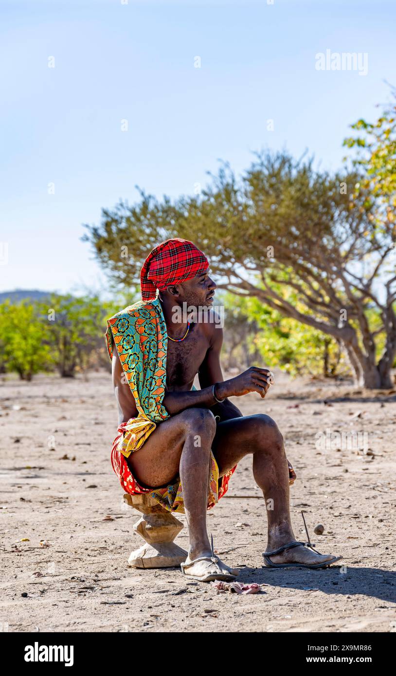 Traditional Hakaona man sitting on a stool, Angolan tribe of the Hakaona, near Opuwo, Kunene, Namibia Stock Photo