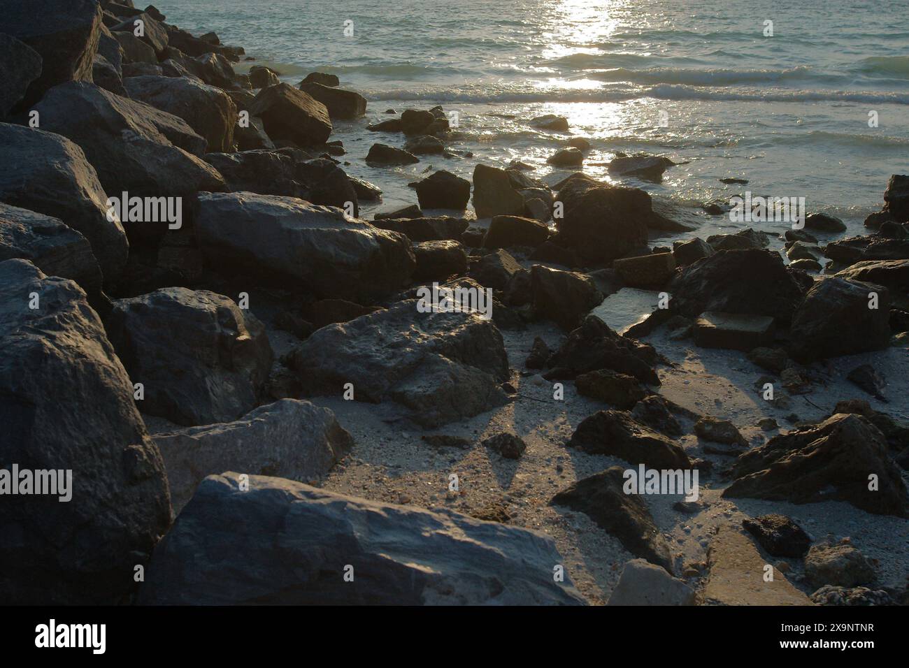 Medium view Large Rocks on edge of water shoreline near sunset in Florida. Multi colors and waves rolling in at about 45 degrees. Sunlight shade Stock Photo