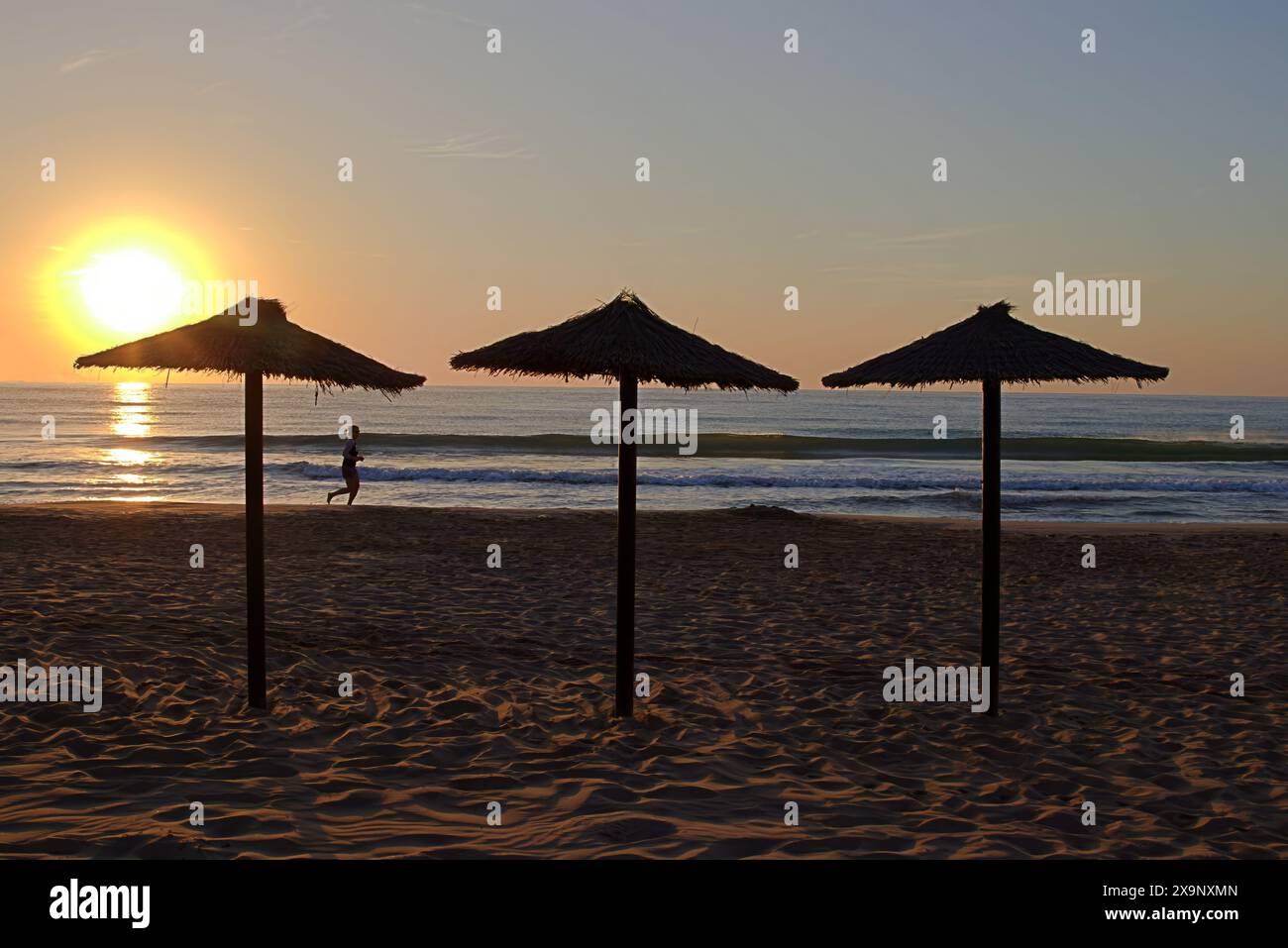 Beach umbrellas at sunrise with jogger silhouette Stock Photo