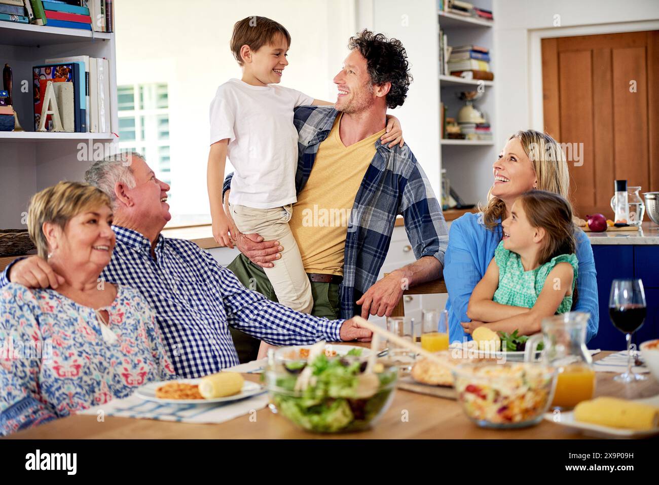 Lunch, happy family and food in living room for nutrition, bonding and healthy meal and drink. Parents, kids and grandparents with smile at table for Stock Photo