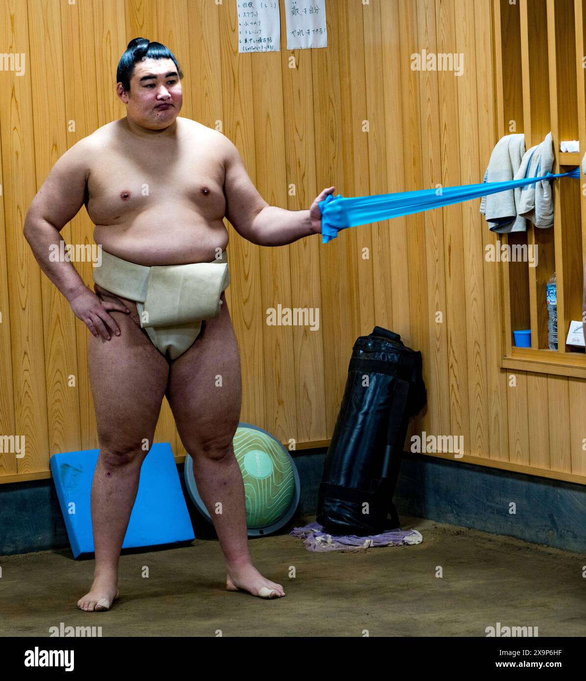 Sumo wrestler in mawashi exercises with a resistance band indoors Stock Photo