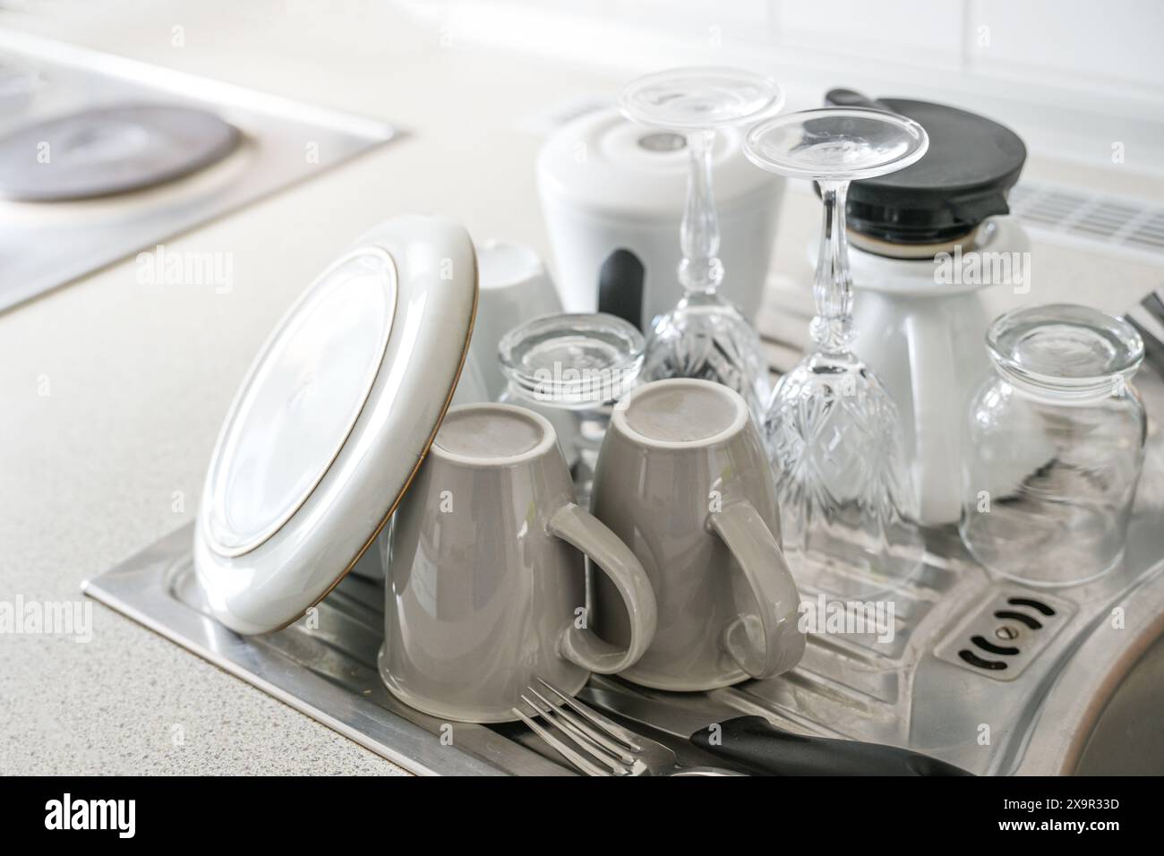 Washed dishes set out to dry next to the sink in the kitchen in a minimalist household without a dishwasher, water-saving and ecological, copy space, Stock Photo