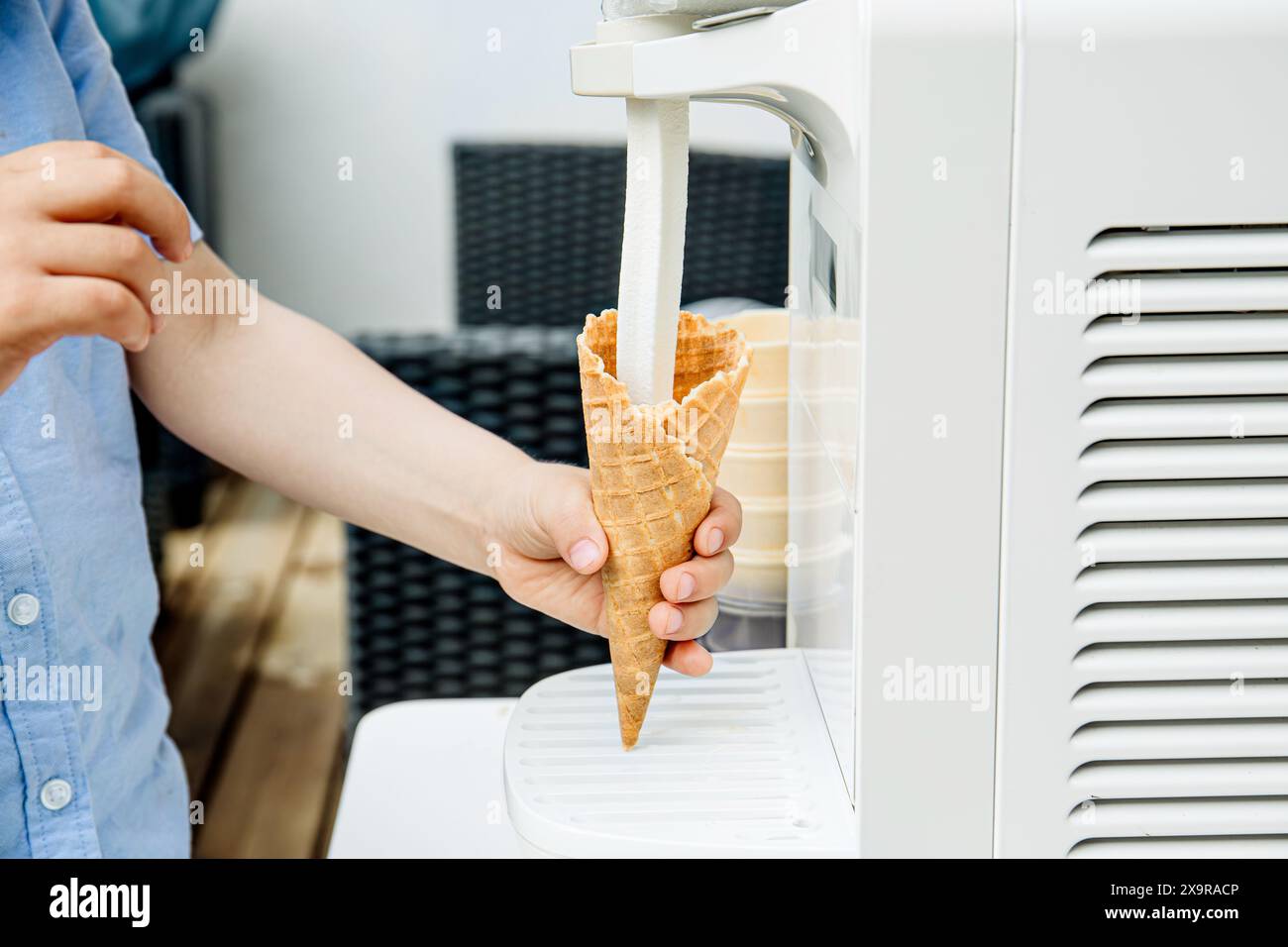 Close up view of child hand using home use ice cream maker machine. Making soft serve ice cream and pouring in cone outdoors in garden yard. Stock Photo
