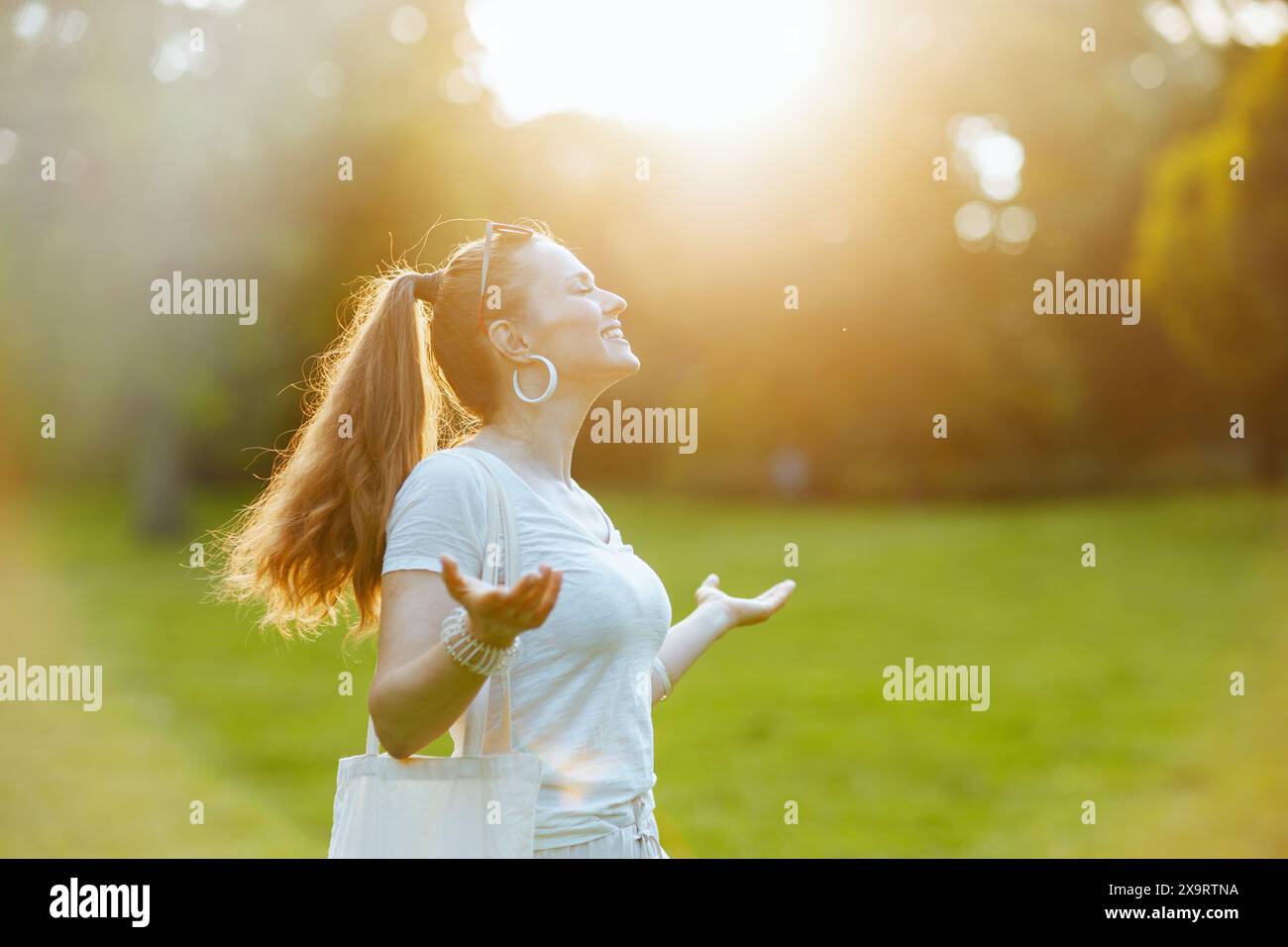 Summer time. happy modern 40 years old woman in white shirt enjoying in the meadow outside in nature. Stock Photo