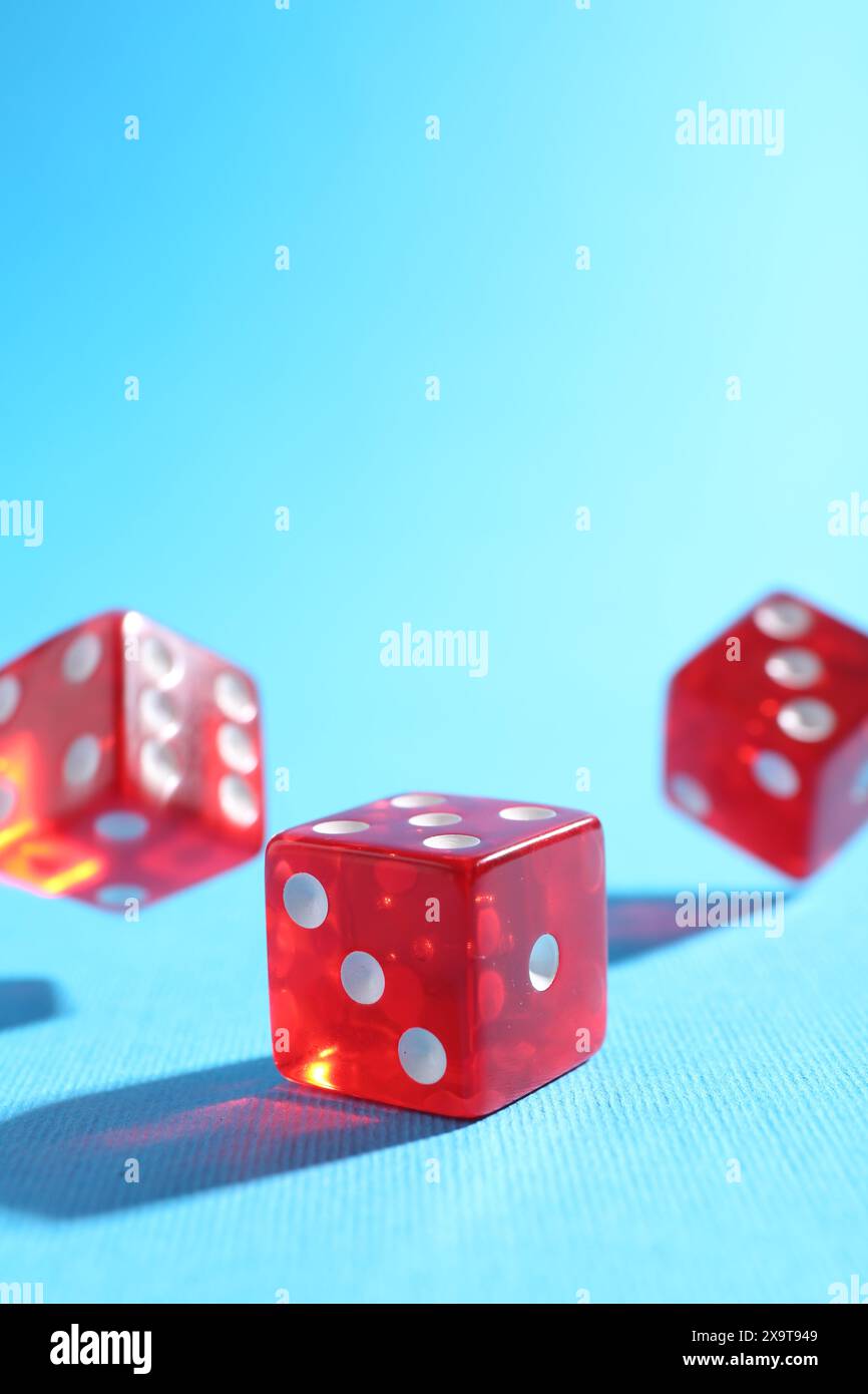Three red game dices falling on light blue background, closeup Stock Photo