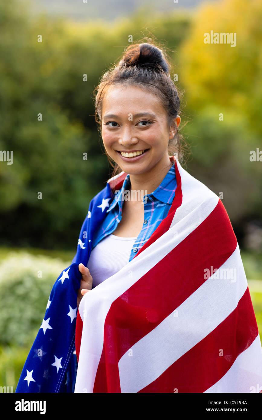 Portrait of happy asian woman covered with flag of usa in garden Stock Photo