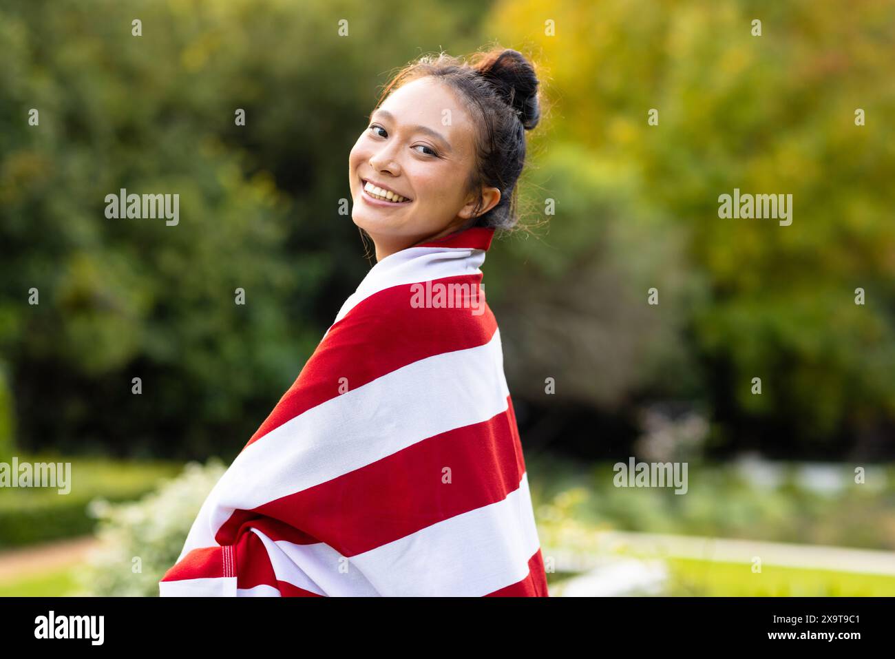 Portrait of happy asian woman covered with flag of usa in garden Stock Photo