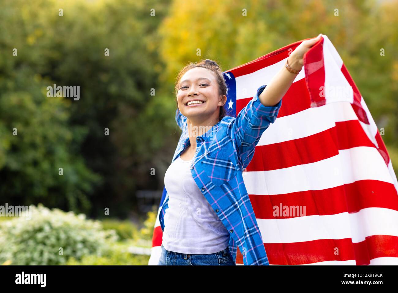 Portrait of happy asian woman covered with flag of usa in garden Stock Photo