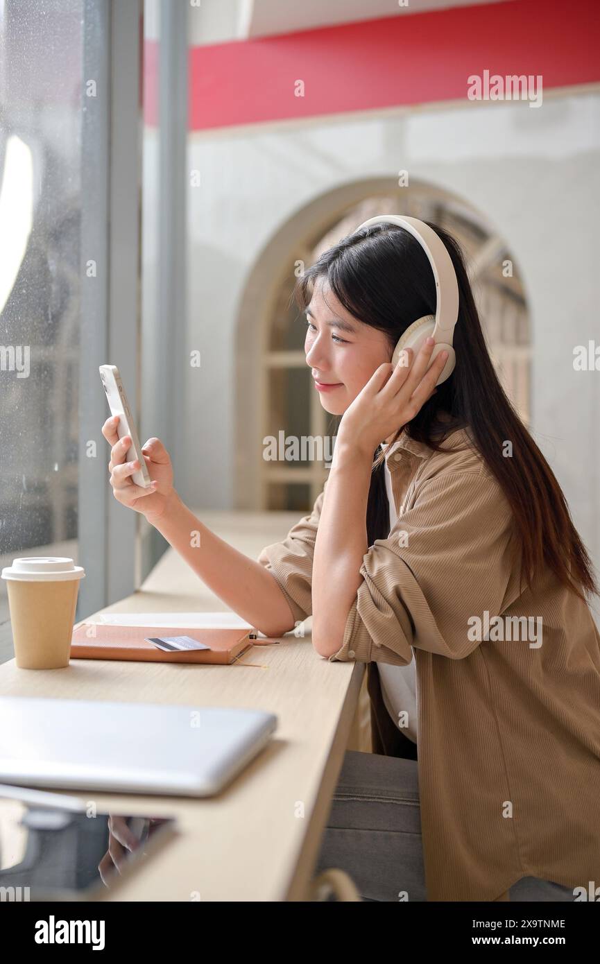 An attractive, happy young Asian woman is scrolling on her smartphone ...