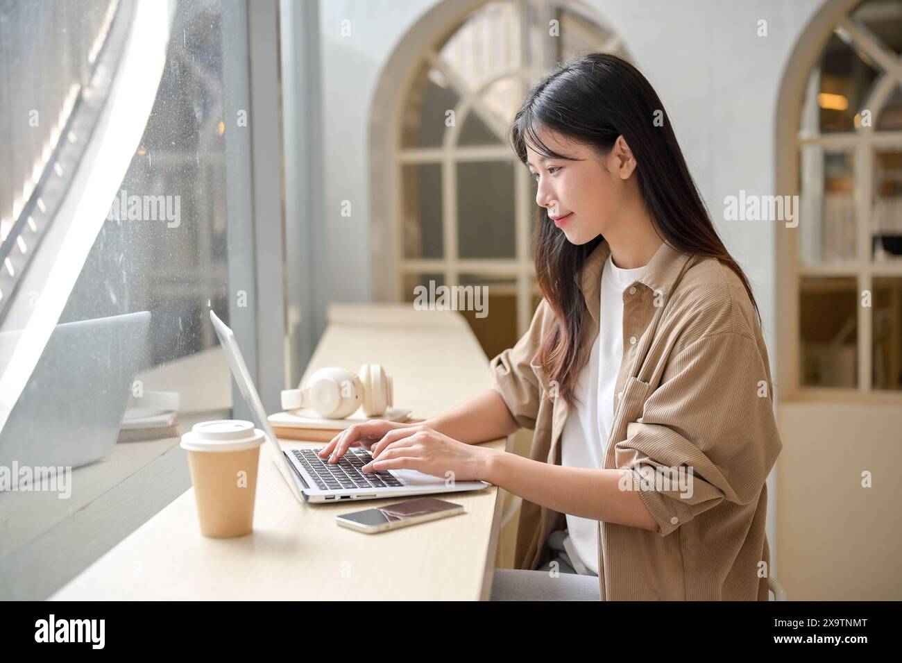 An attractive young Asian woman is working remotely from a coffee shop ...