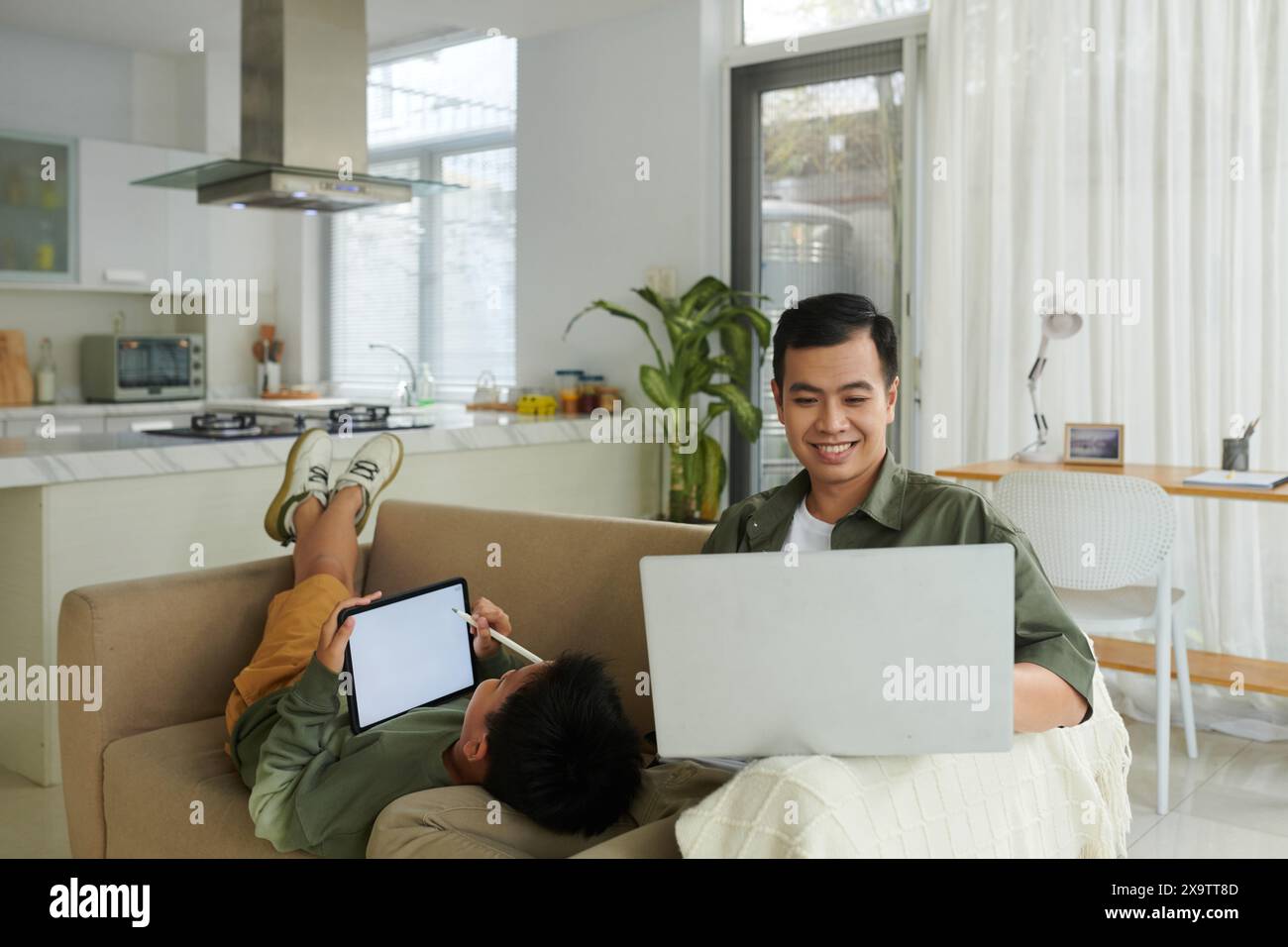 Smiling man working on laptop from home when son drawing on tablet screen Stock Photo