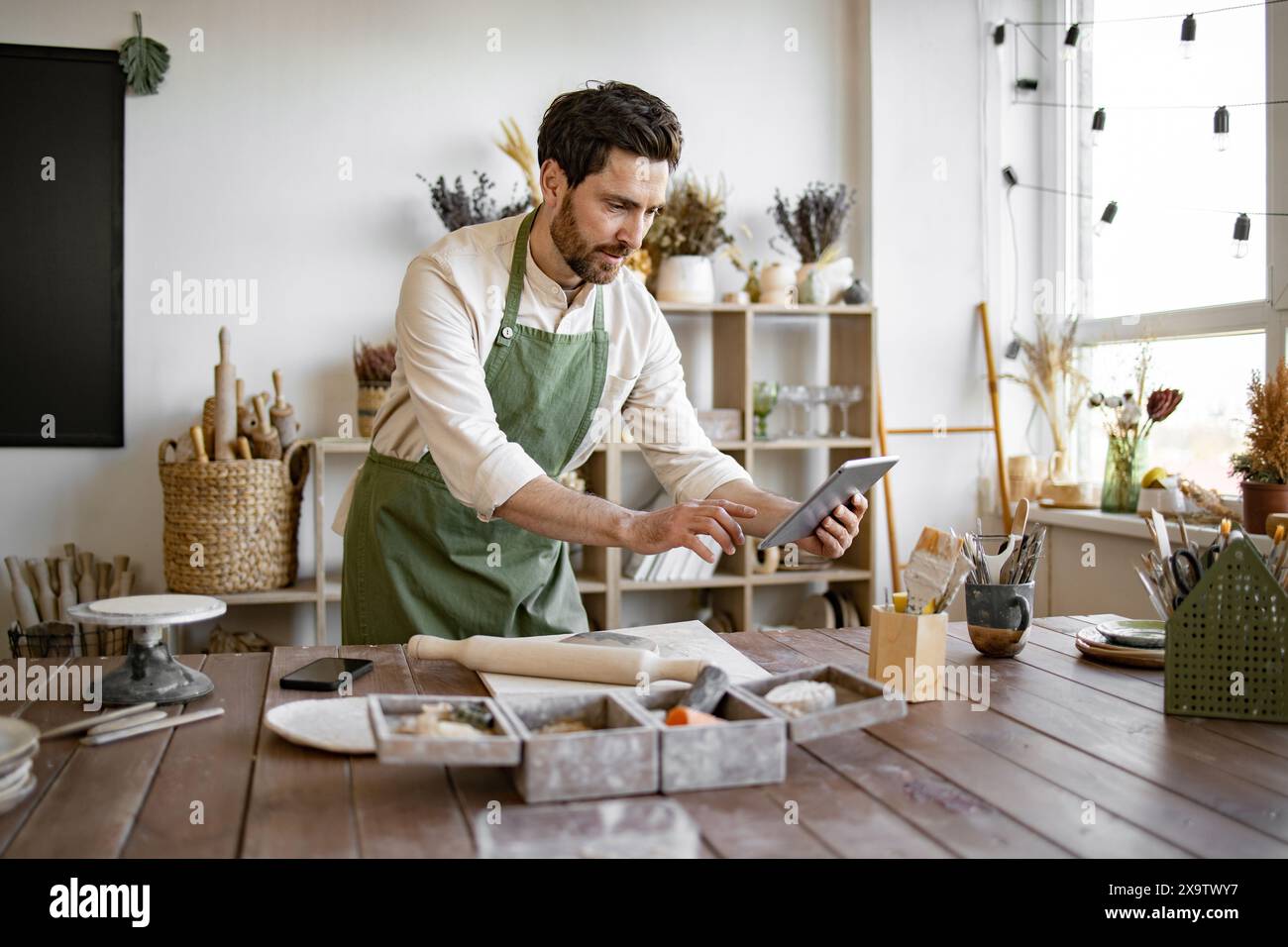 Bearded adult man in apron and white shirt viewing an online course Stock Photo