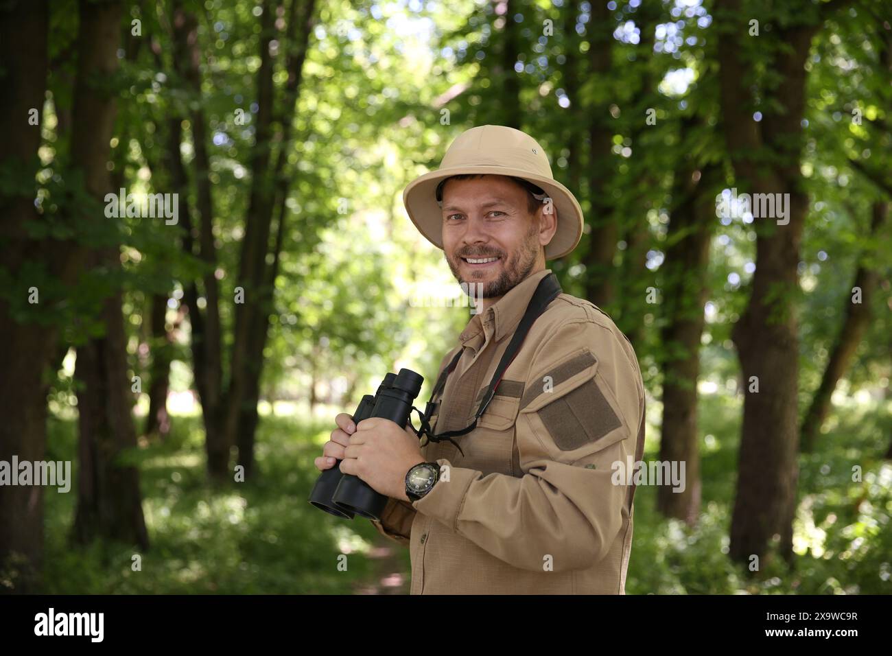 Forester with binoculars examining plants in forest Stock Photo