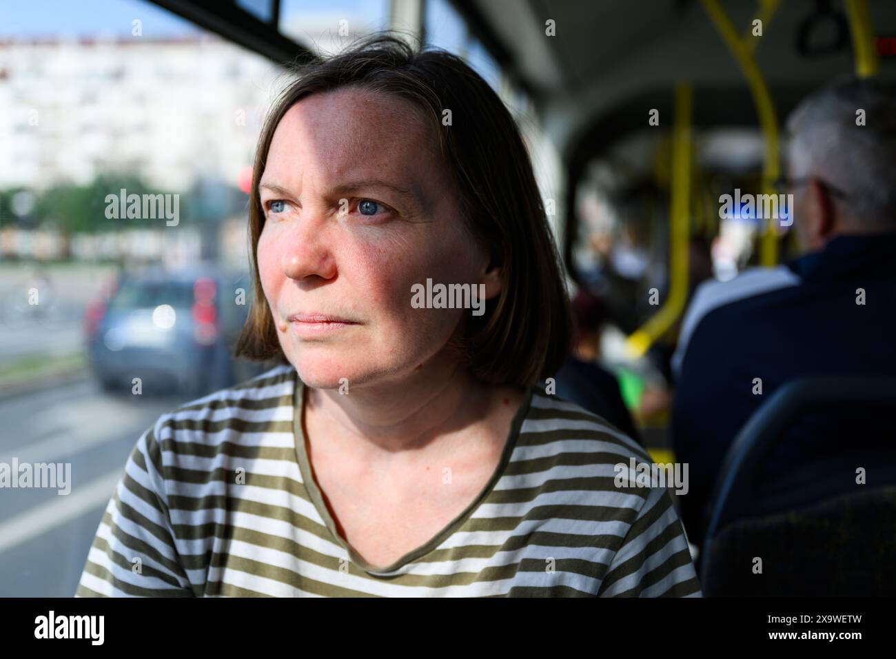 Portrait of serious adult caucasian brunette female looking out the bus window while using public transportation to travel through the city, selective Stock Photo