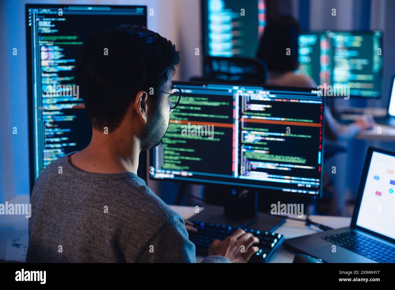 Asian software developers working on multiple screens displaying code and application diagrams at night in modern office Stock Photo
