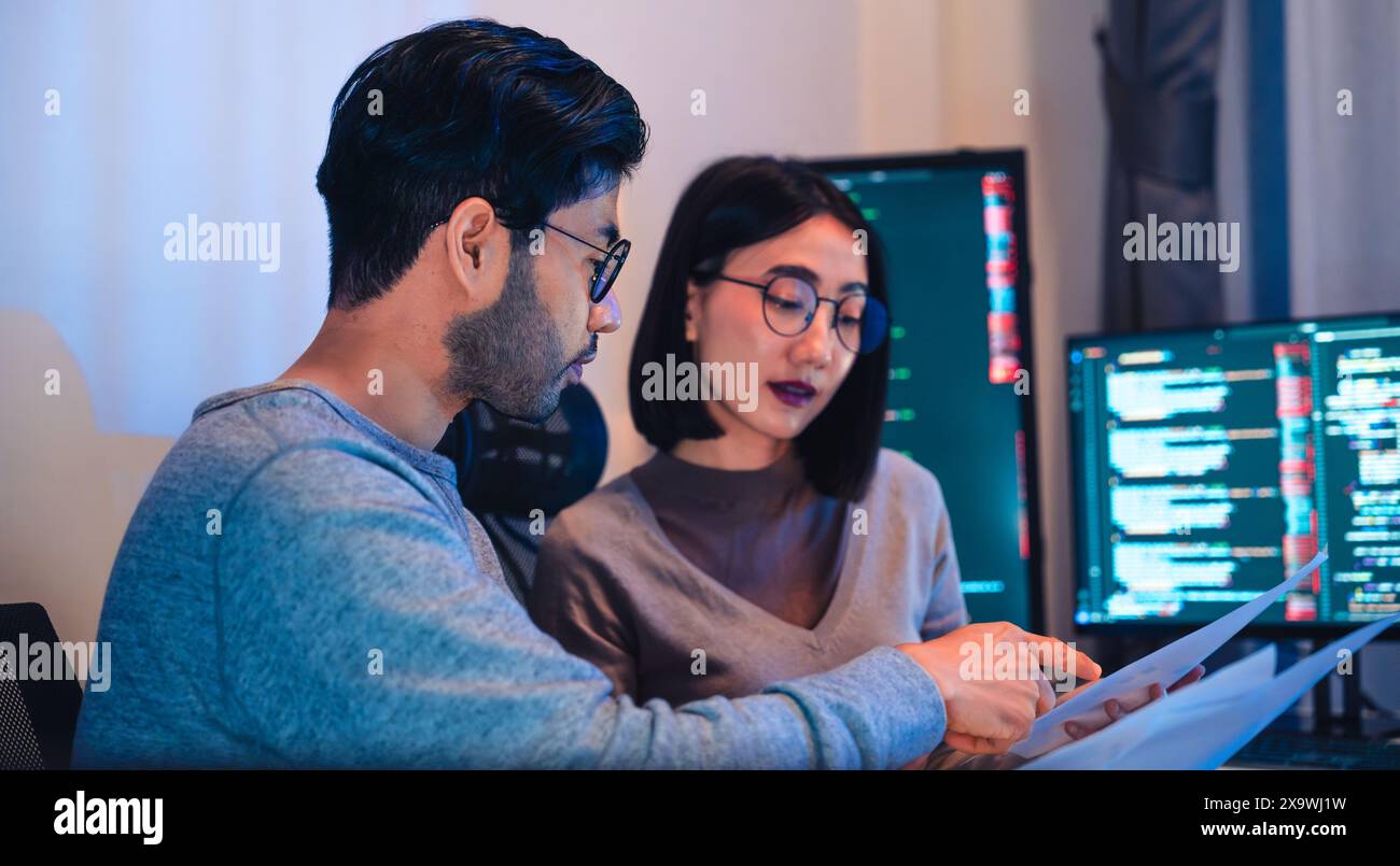 Asian software developers teams working on multiple screens displaying code and application diagrams at night in modern office Stock Photo