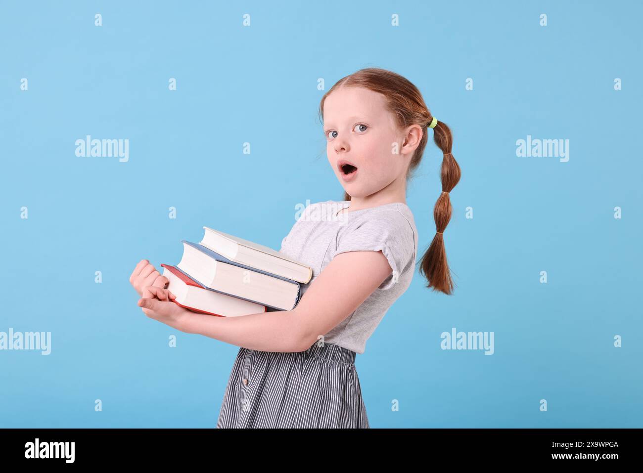 Surprised girl with stack of books on light blue background Stock Photo ...