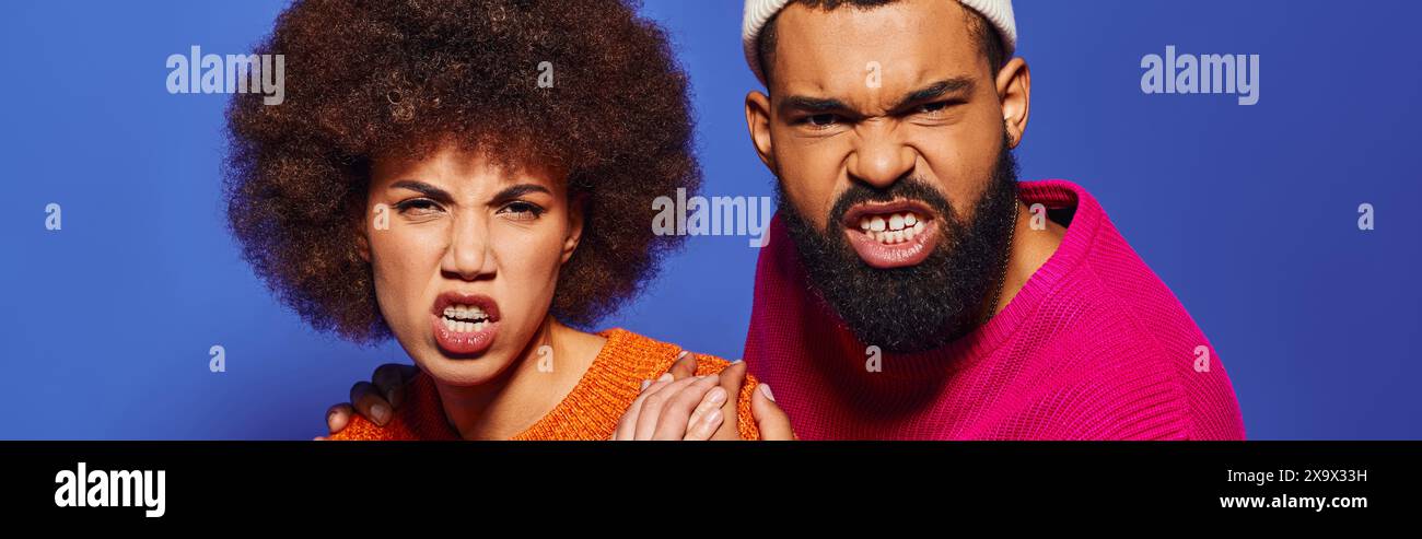 A young African American man and woman in vibrant attire, expressing emotions on a blue background. Stock Photo
