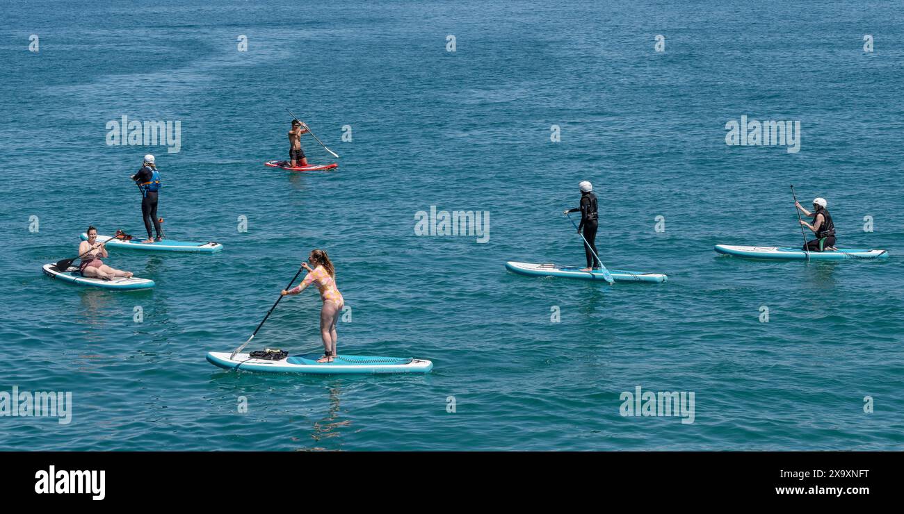 A panoramic image of holidaymakers using stand up paddleboards in Newquay Bay in Cornwall. Stock Photo