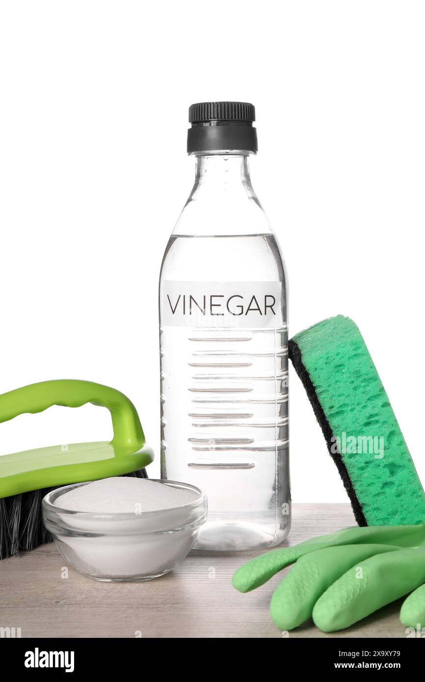 Natural cleaning products. Vinegar in bottle, baking soda, glove, sponge and brush on light wooden table against white background Stock Photo