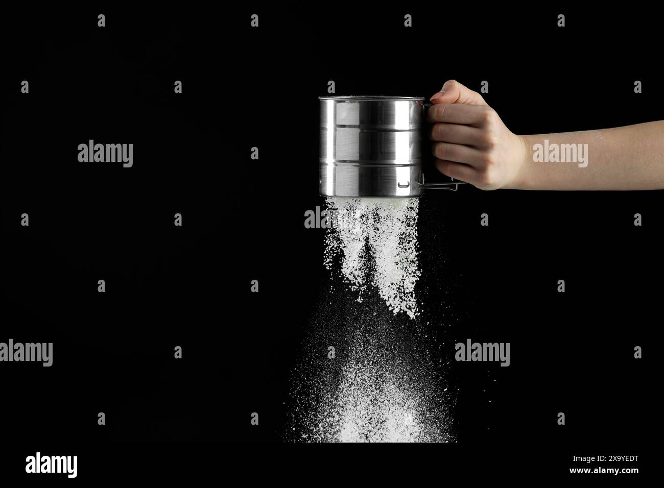 Woman sieving flour against black background, closeup. Space for text ...