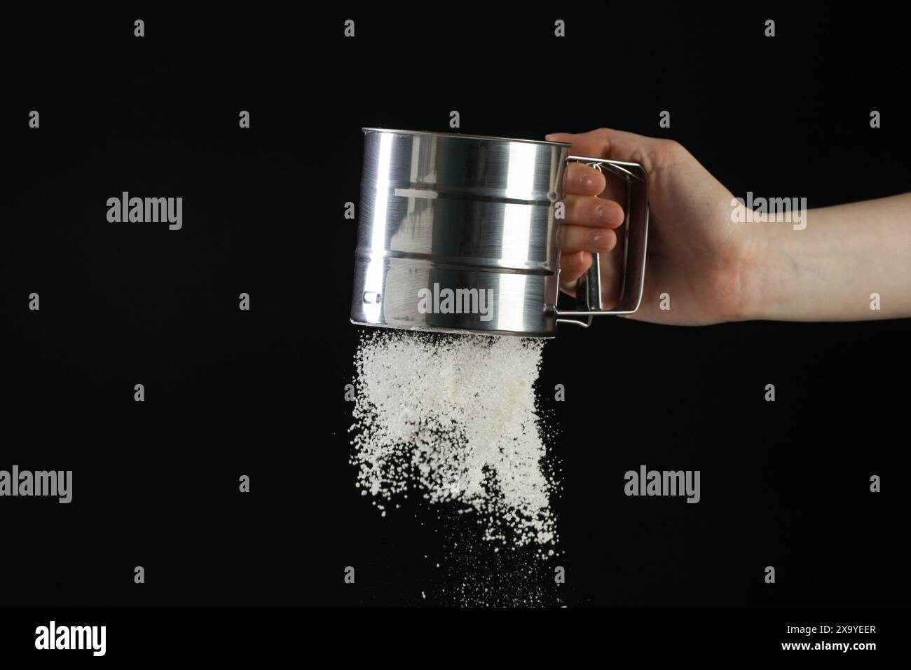 Woman sieving flour against black background, closeup. Space for text ...