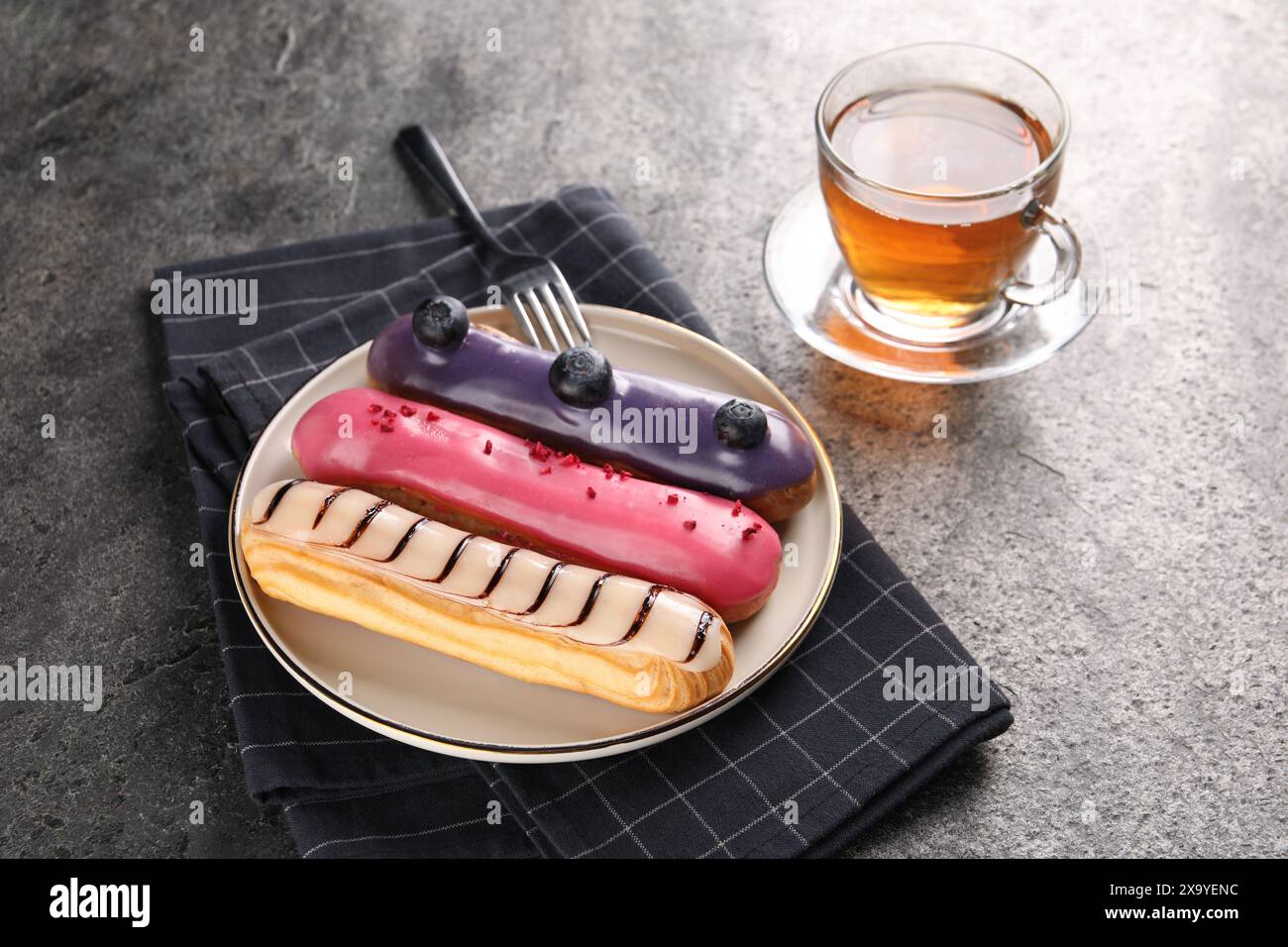 Different tasty glazed eclairs served with tea on grey textured table Stock Photo