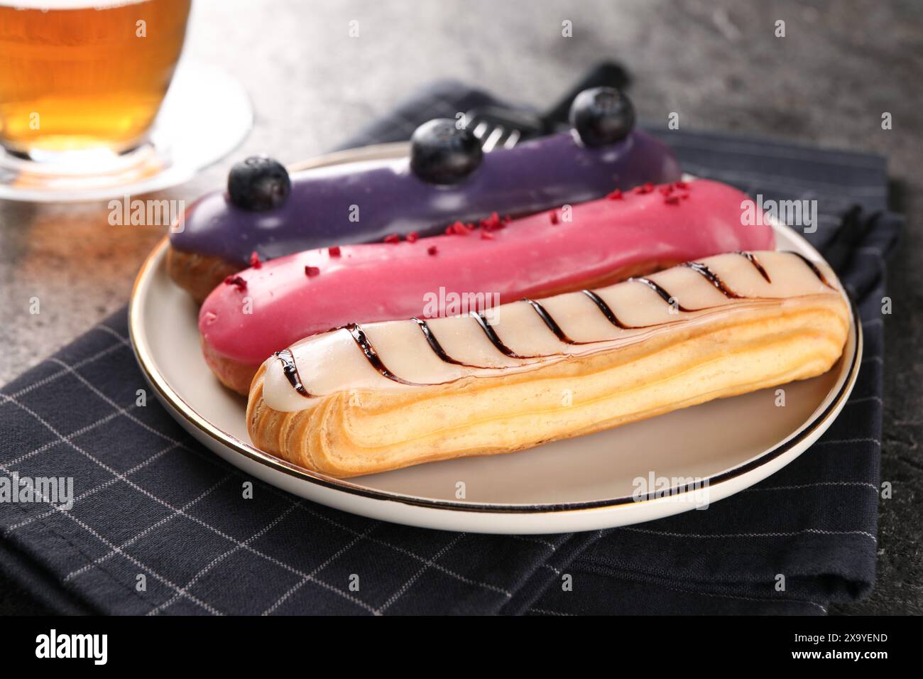Plate with different tasty glazed eclairs on table, closeup Stock Photo