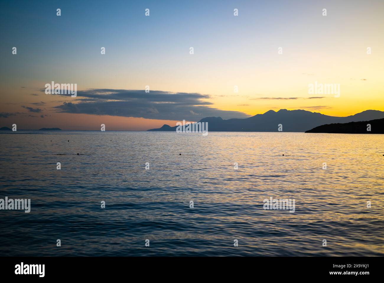 Sun setting over tranquil sea and mountains Stock Photo