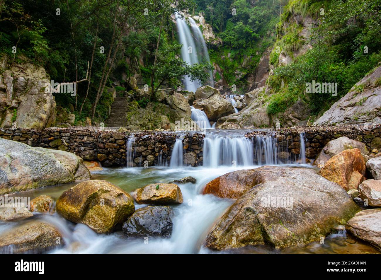 A waterfall cascading through rocky terrain surrounded by lush greenery ...