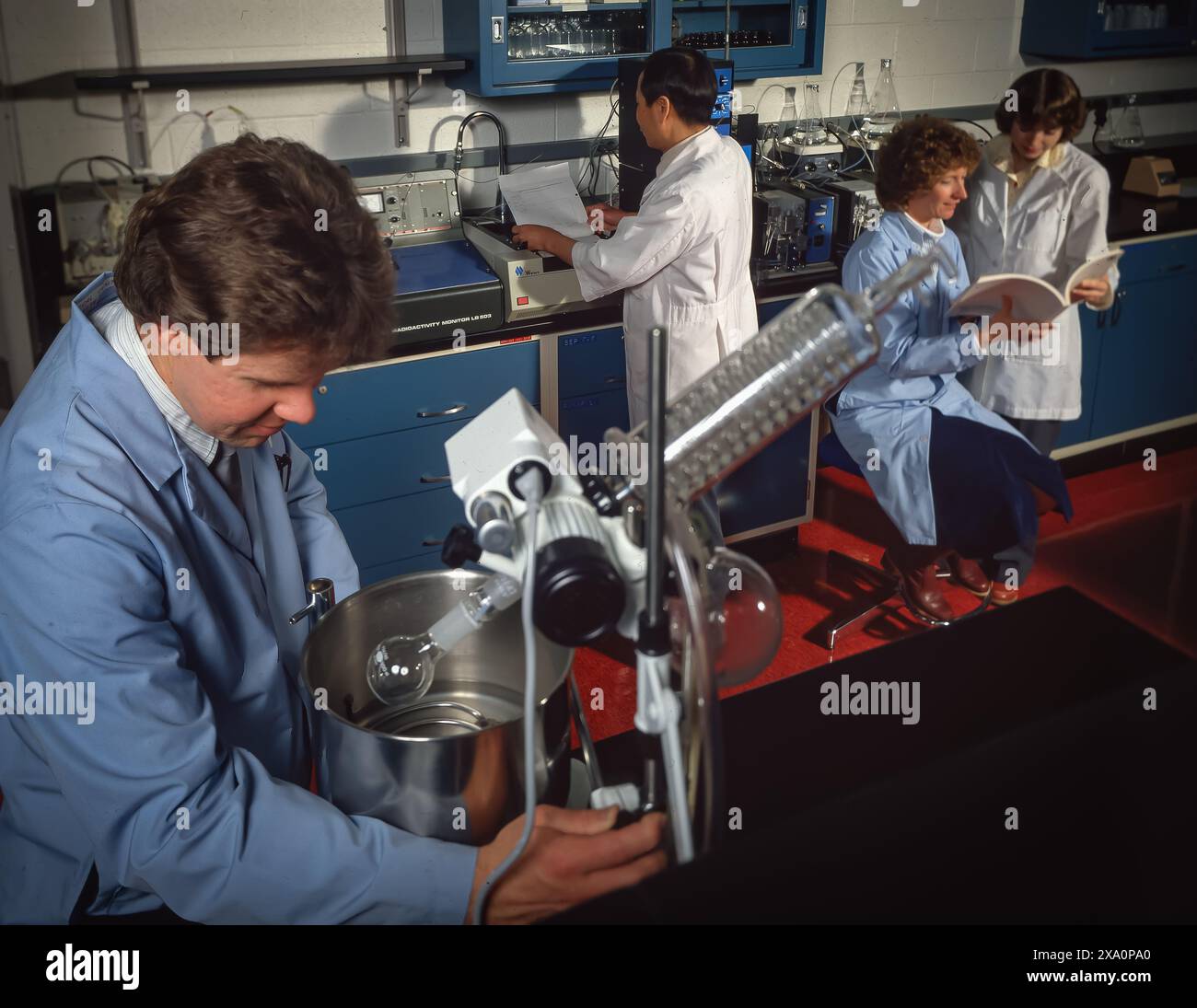 Students and instructor working in a laboratory, conducting experiments with glassware and equipment while reviewing notes in a modern science lab. Stock Photo