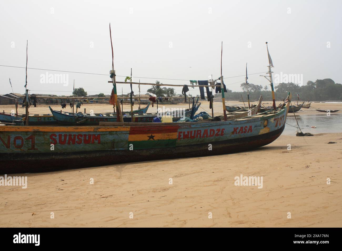 A large, brightly painted fishing boat rests on the sandy beach of a Ghanaian coastal village. The vibrant colors and detailed artwork on the boat ref Stock Photo