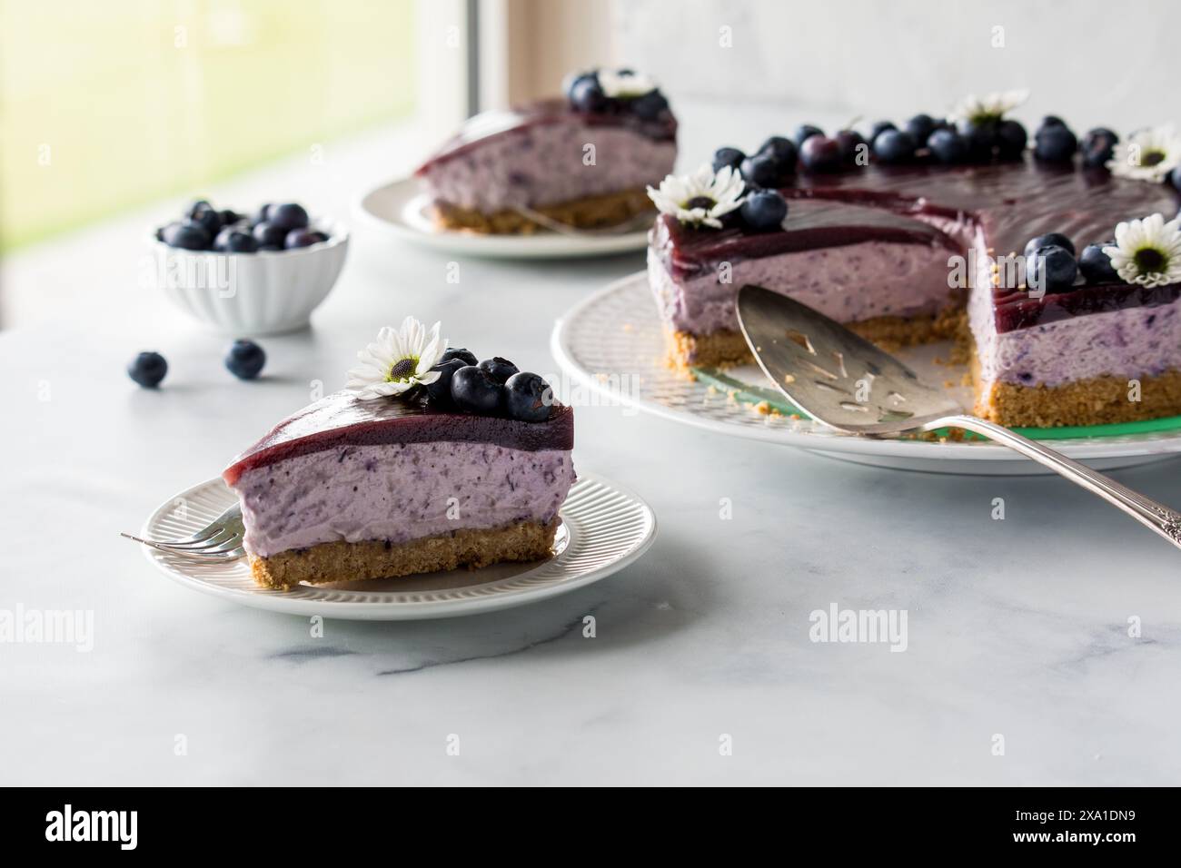 Slices of creamy blueberry cheesecake next to a sunny window. Stock Photo