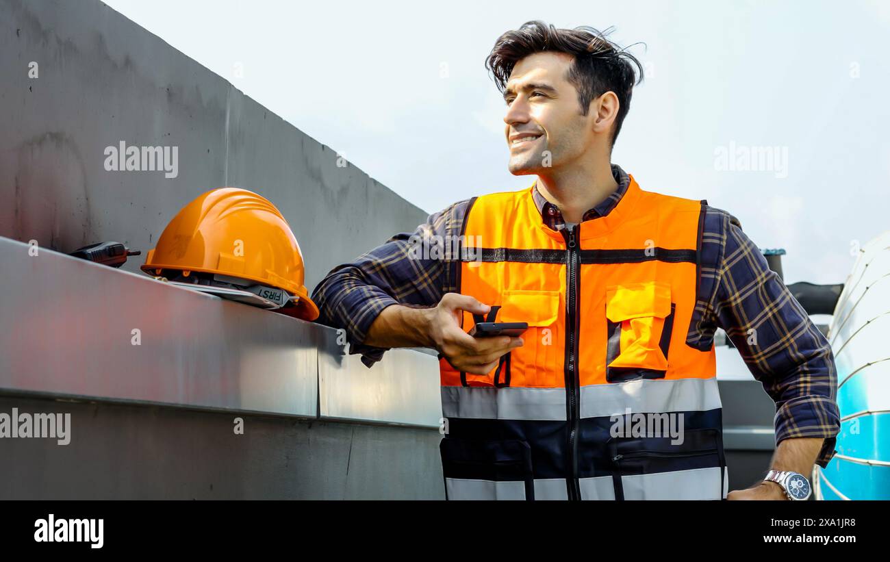 A man stands in front of a metal wall with a helmet on shoulder. Stock Photo